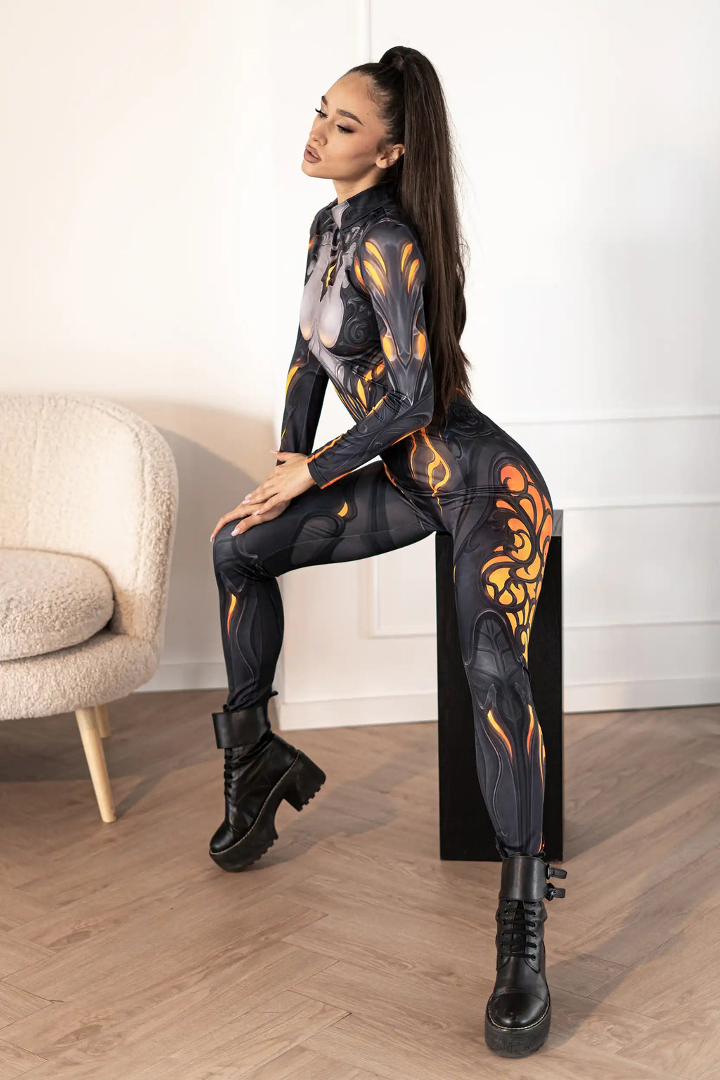 Woman wearing a black and orange flame-patterned outfit sitting on a chair.