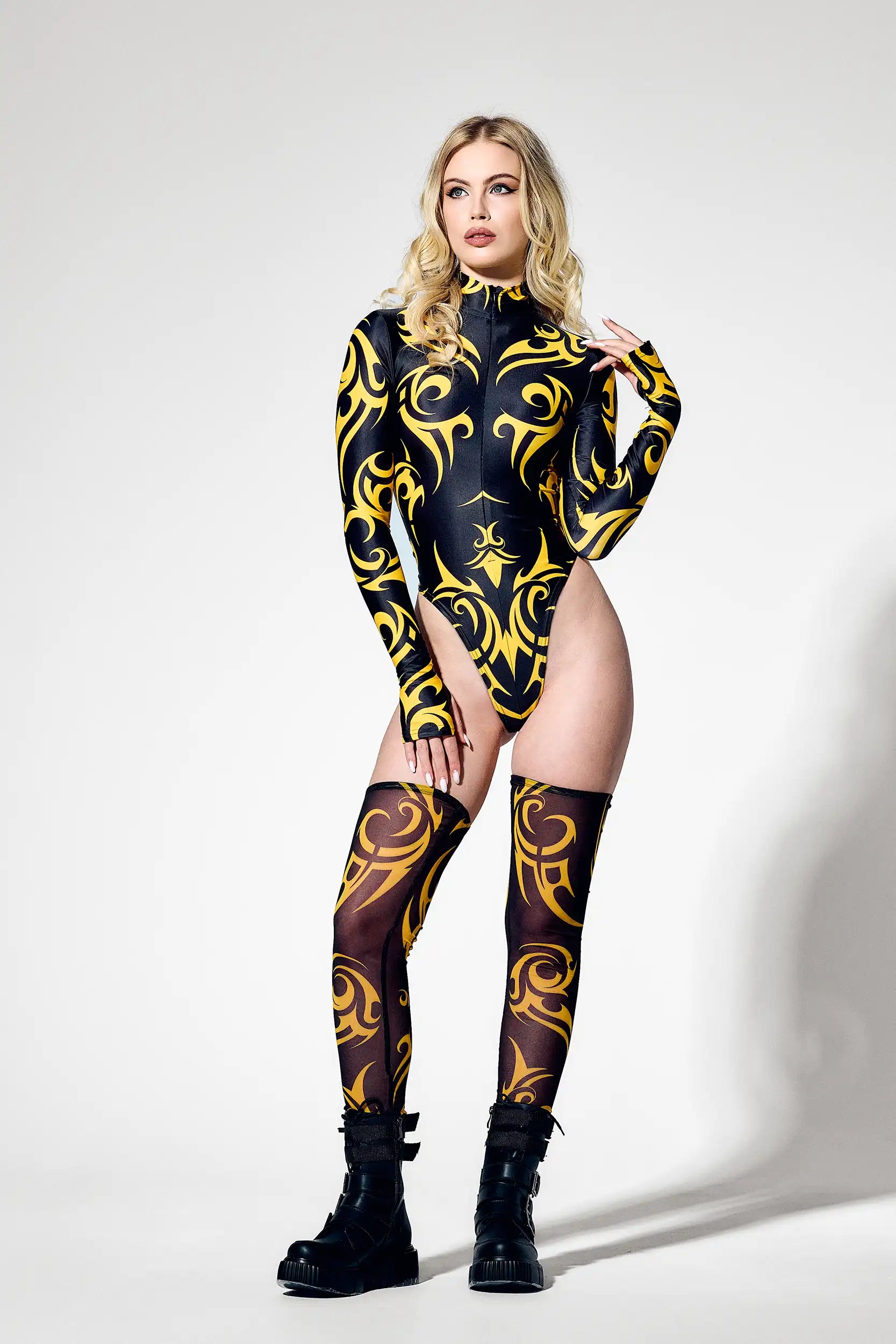 Woman wearing a black and yellow patterned bodysuit with matching stockings and boots on a white background