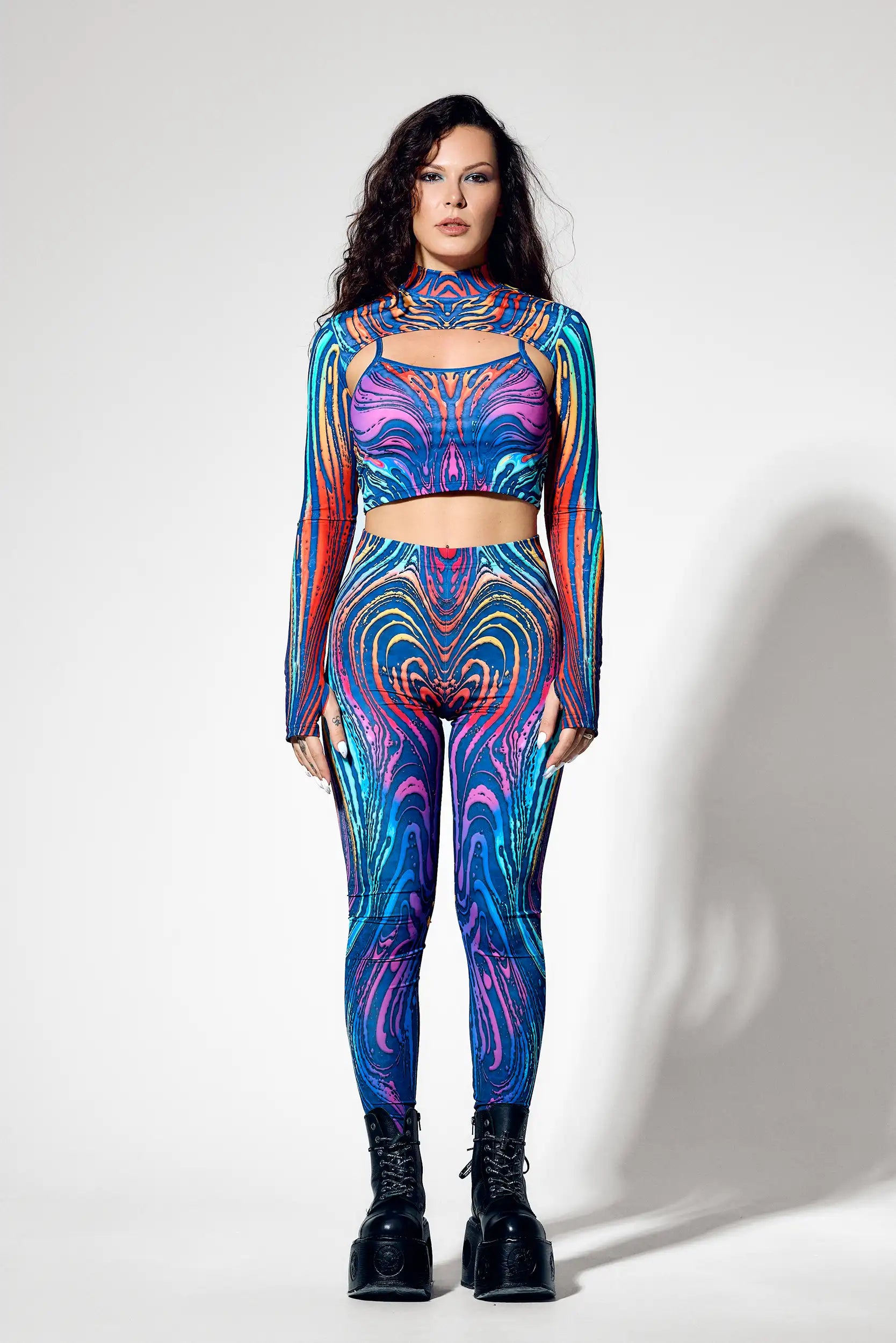 Woman wearing psychedelic three piece rave set with crop top shrug and leggings