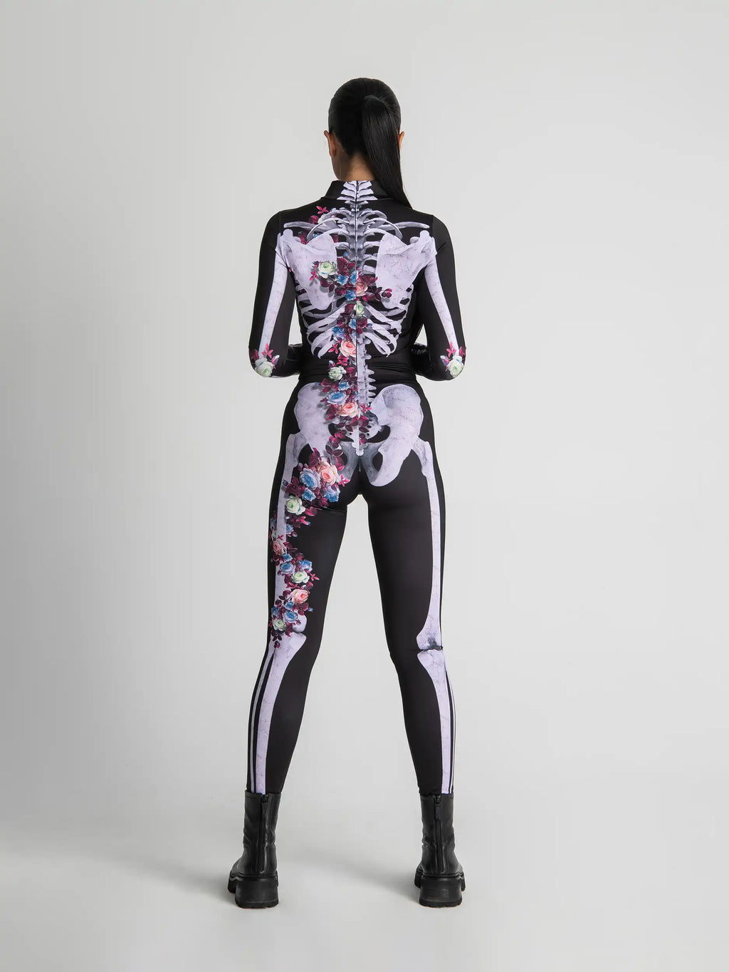 Person wearing a black and white skeleton-themed bodysuit with colorful floral patterns on a gray background
