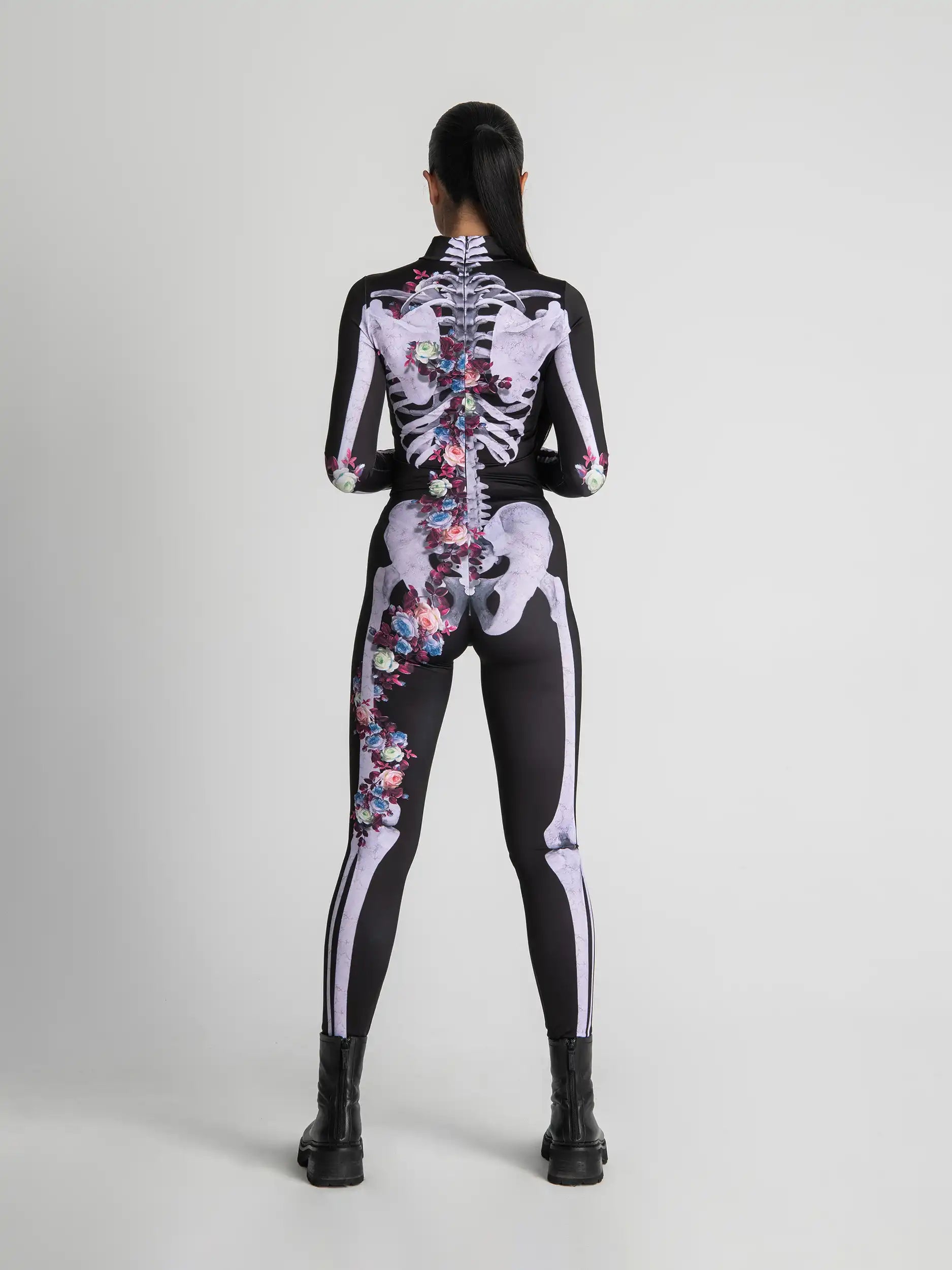 Person wearing a black and white skeleton-themed bodysuit with colorful floral patterns on a gray background