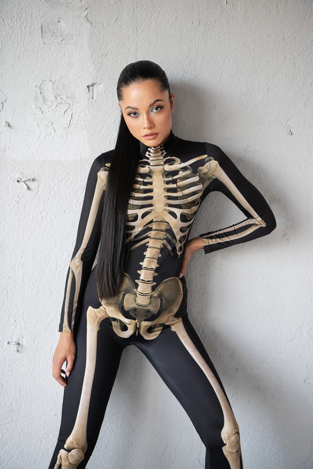 Person wearing a black and beige skeleton costume against a white wall.