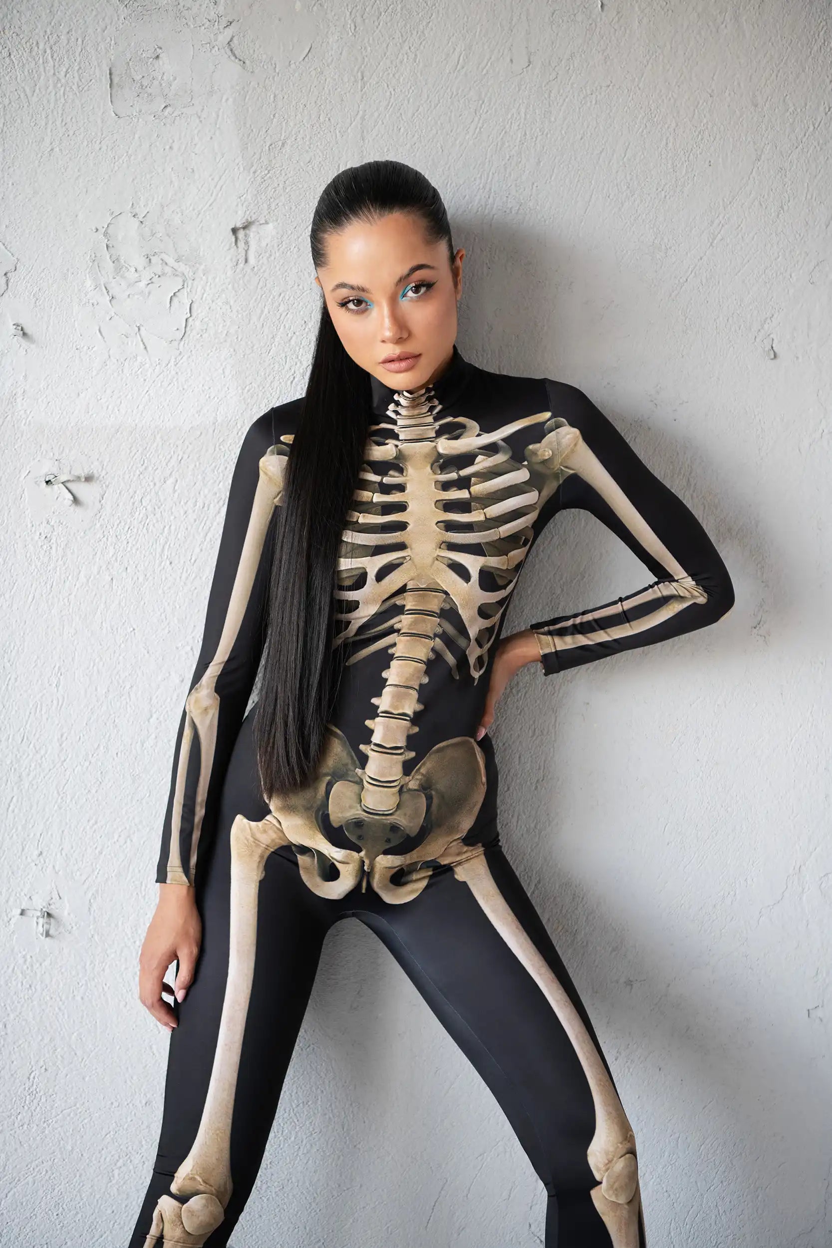 Person wearing a black and beige skeleton costume against a white wall.